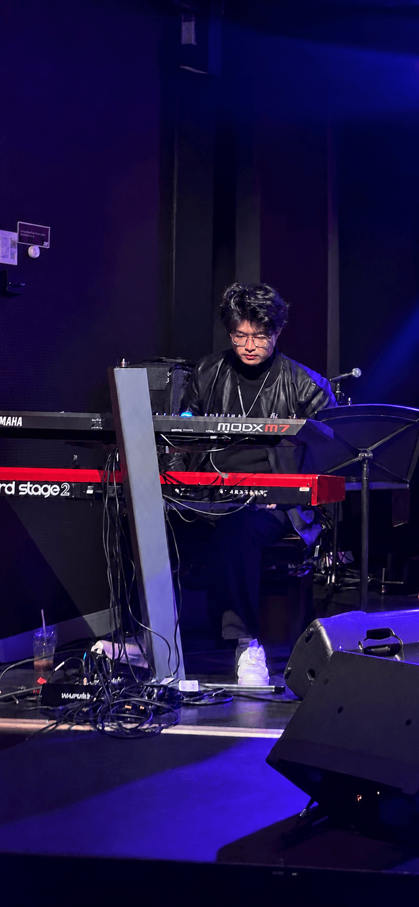 Botian Ye performing keyboard vocals beside a microphone in a warm Sydney evening venue.